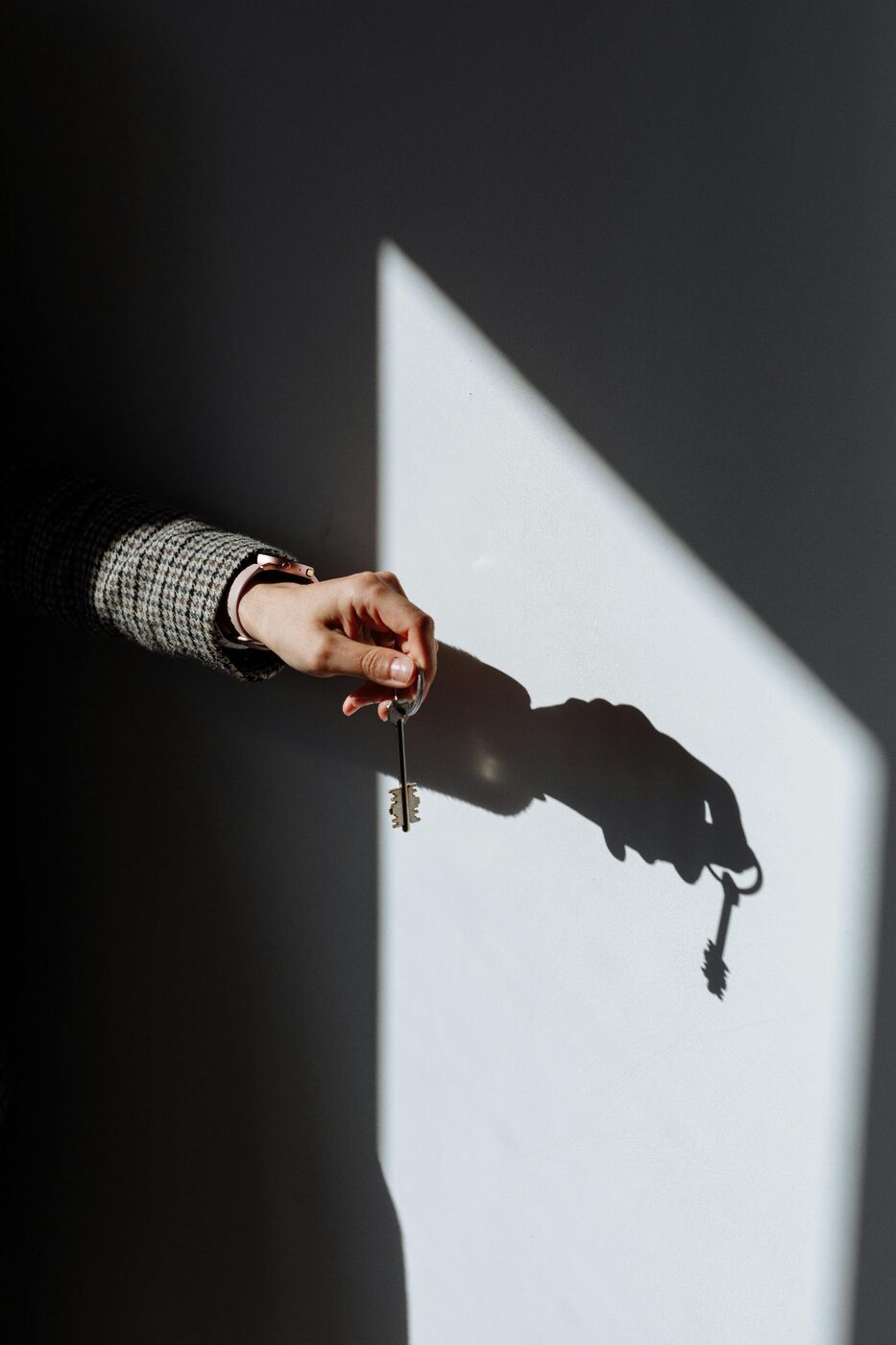 Black and white photo of a hand holding a key casting a shadow on a wall